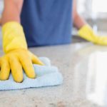 Person with yellow gloves cleaning a granite countertop using a soft cloth