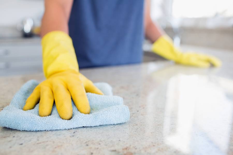 Person with yellow gloves cleaning a granite countertop using a soft cloth - Granite Bathroom Countertops Installation in Delray Beach and Fort Pierce